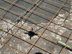 Exposed concrete section showing wood framing, dirt, and a Wavelogix sensor with wire